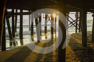 Sunset from under a pier with a surfer in the middle