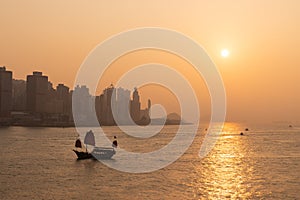Sunset in Victoria Harbour, Hong Kong with cityscape of Sheung Wan and Kennedy Town. with tourist junk in the golden sea