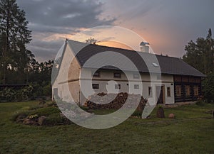 Sunset view of half timbered masonry, old rustic cottage house with chopped wood in summer garden with flowers, rock and