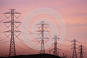 Sunset view of high voltage electricity towers on the hills of San Francisco bay area; Wind turbines visible in the background;