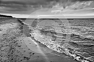 at sunset, a view over the beach in Zingst on the Baltic Sea. Walk along the sea in black and white. Moving clouds in the sky