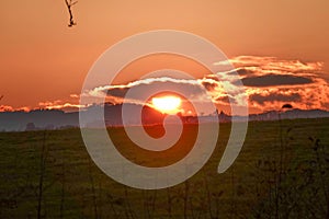 Sunset view over the field red sun setting behind clouds making sky golden