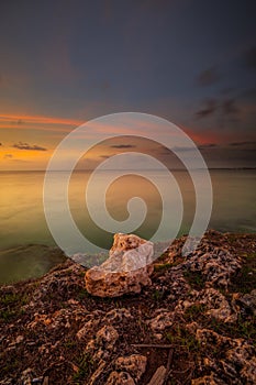 Sunset view. Seascape background. Amazing ocean view. Beach with rocks and stones. Bright sunlight on horizon line. Cloudy sky.