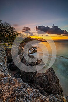 Sunset view. Seascape background. Amazing ocean view. Beach with rocks and stones. Bright sunlight on horizon line. Cloudy sky.
