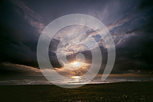 Sunset view, seashore, stormy waves, heavy rain clouds on horizon, sun breaking through the cloud like an eye