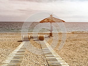 Sunset view on straw umbrella on sea sandy tropical beach with reed paths rolled up on sunny day, idyllic picture of relaxing on