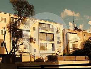 Sunset view of a vintage urban apartment building in Tel Aviv, Israel, with a silhouette of a tree and golden sunlight
