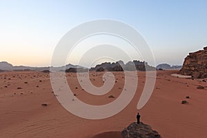 Sunset in the Wadi Rum desert, Jordan, with a man watching the scene from a rock on foreground