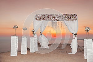 Sunset. Wedding ceremony arch with flowers decorative arrangement and white curtain on cliff above sea, sunrise outdoor summer ph