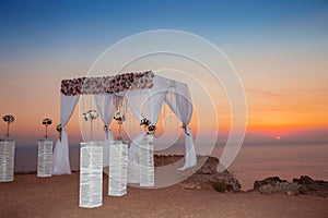 Sunset. Wedding ceremony arch with flowers decorative arrangement and white curtain on cliff above sea, sunrise outdoor summer ph