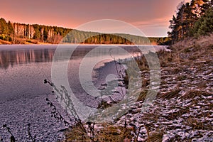 sunset in the winter forest. forest on the banks of the frozen river. ice on the river