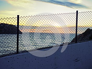 Sunset through wire fence. Pink sunset on promenade