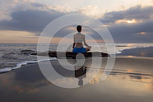 Sunset yoga. Caucasian woman sitting on the stone in Lotus pose. Padmasana. Hands in gyan mudra. Beach in Bali. View from back.