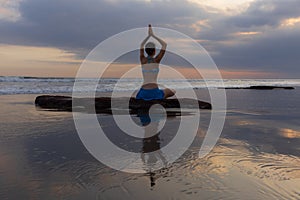 Sunset yoga. Caucasian woman sitting on the stone in Lotus pose. Padmasana. Hands in namaste mudra. Bali beach. View from back.