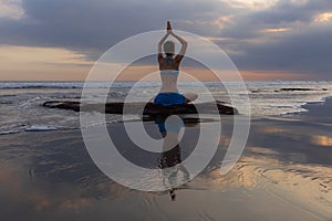 Sunset yoga. Caucasian woman sitting on the stone in Lotus pose. Padmasana. Hands in namaste mudra. Bali beach. View from back.