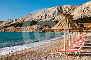 Sunshades and orange deck chairs on beach at Baska - Krk