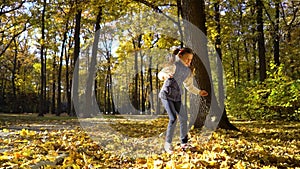 Sunshine on cute little girl throwing yellow leaves up in the air in autumn park