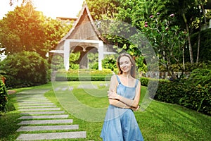 Sunshine portrait of young woman looking at camera smiling on green palms and house background in Thailand