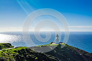 Sunshine pouring over Cape Reinga Lighthouse, azure surface of calm ocean behind. Famous tourist attraction at Cape