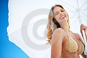 Sunshine and smiles. Portrait of a beautiful young woman holding a beach umbrella on a summers day.