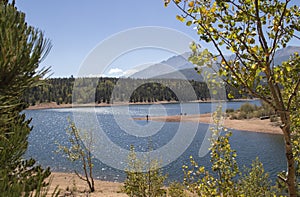 Sunshine sparkles on the water a fisheman stands on a point and aspen leaves turning yellow shimmer at Chrystal Reservoir half way