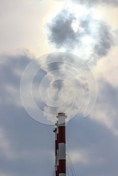 Sunshine struggling through the smoke cloud from three industrial plant chimneys standing in a row