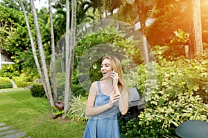 Sunshine young woman talking call with phone and smiling on palms and house background