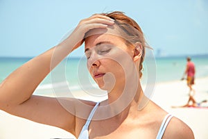Sunstroke woman on sunny beach. Woman with headache. Hot sun danger. Health problem on holiday photo
