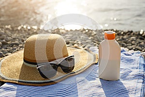 Suntan cream bottle and sunglasses on beach towel with sea shore on background. Sunscreen on deck chair outdoors on