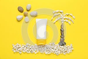 Suntan cream, sun and palm made of marble pebbles on yellow background, flat lay