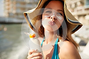 Suntan lotion. Cute woman applying suntan cream sunscreen solar from plastic container bottle on her nose and cheecks