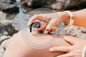 Suntan Lotion. Sexy Woman in bikini apply sun protection cream on her smooth tanned legs. Skin care. Legs on the beach