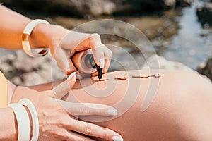 Suntan Lotion. Sexy Woman in bikini apply sun protection cream on her smooth tanned legs. Skin care. Legs on the beach