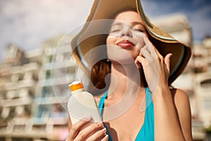 Suntan lotion. Woman applying sunscreen solar cream on face. Beautiful happy cute girl puts suntan cream from plastic