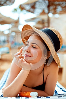 Suntan woman in hat applying sunscreen solar. Beautiful happy woman smear lotion with sun cream to her nose.