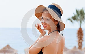 Suntan   woman in hat applying sunscreen solar. Beautiful happy woman smear  lotion  with sun cream   to her nose.