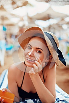 Suntan   woman in hat applying sunscreen solar. Beautiful happy woman smear  lotion  with sun cream to her nose.