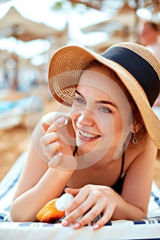 Suntan woman in hat applying sunscreen solar. Beautiful happy woman smear lotion with sun cream to her nose.Ski care