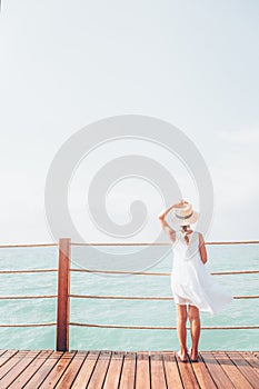 Suntanned girl in white dress enjoyes sea view at the wooden pier