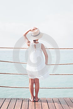 Suntanned girl in white dress enjoyes sea view at the wooden pier