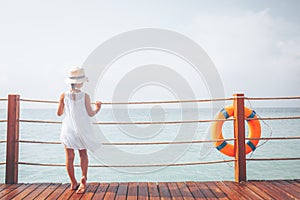 Suntanned girl in white dress enjoyes sea view at the wooden pier