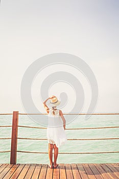 Suntanned girl in white dress enjoyes sea view at the wooden pier