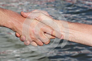 Suntanned male hands make handshake against a water