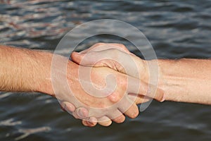 Suntanned male hands make handshake against a water surface