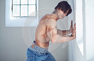 Suntanned muscular male in blue jeans posing.