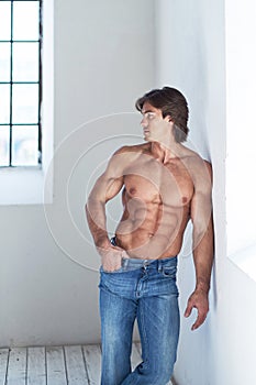 Suntanned muscular male in blue jeans posing.