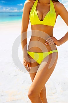 Suntanned woman body in yellow swimsuit against the beach