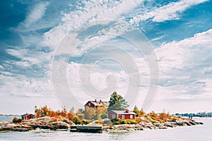 Suomi Or Finland. Beautiful Red Finnish Wooden Log Cabin House On Rocky Island Coast In Summer Sunny Evening. Lake Or