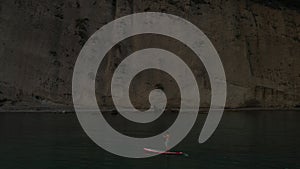 Sup surfer floating standing on paddle sup board on background steep cliff