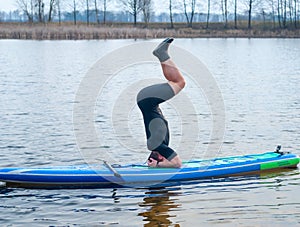 SUP YOGA, a man in a wetsuit doing yoga on a cloudy day, headstand on a paddle Board